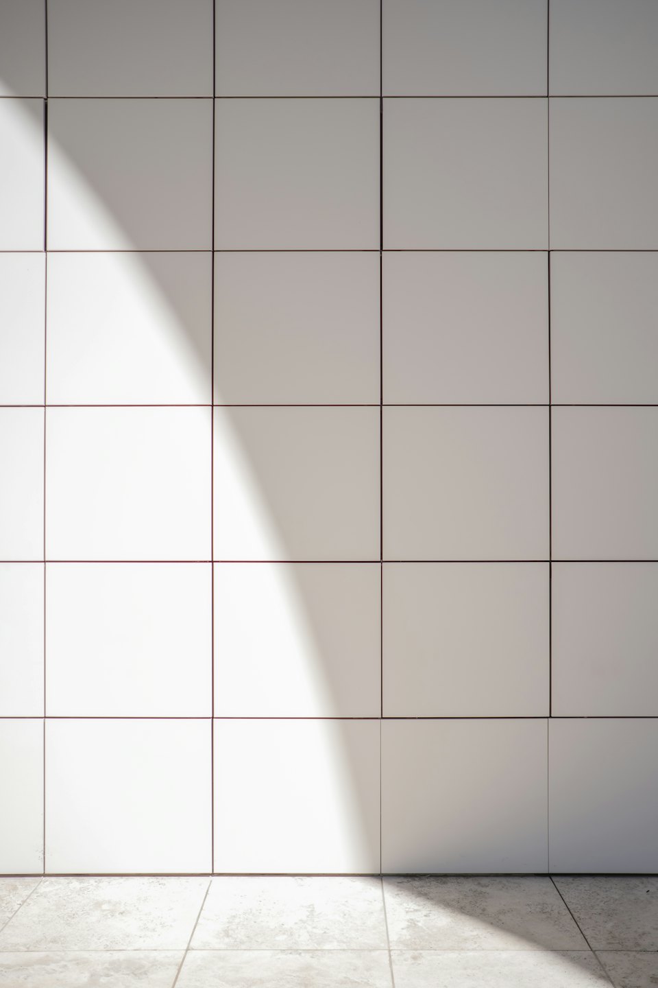 Zonlicht dat op een muur en vloer van lichte vierkante tegels valt.
