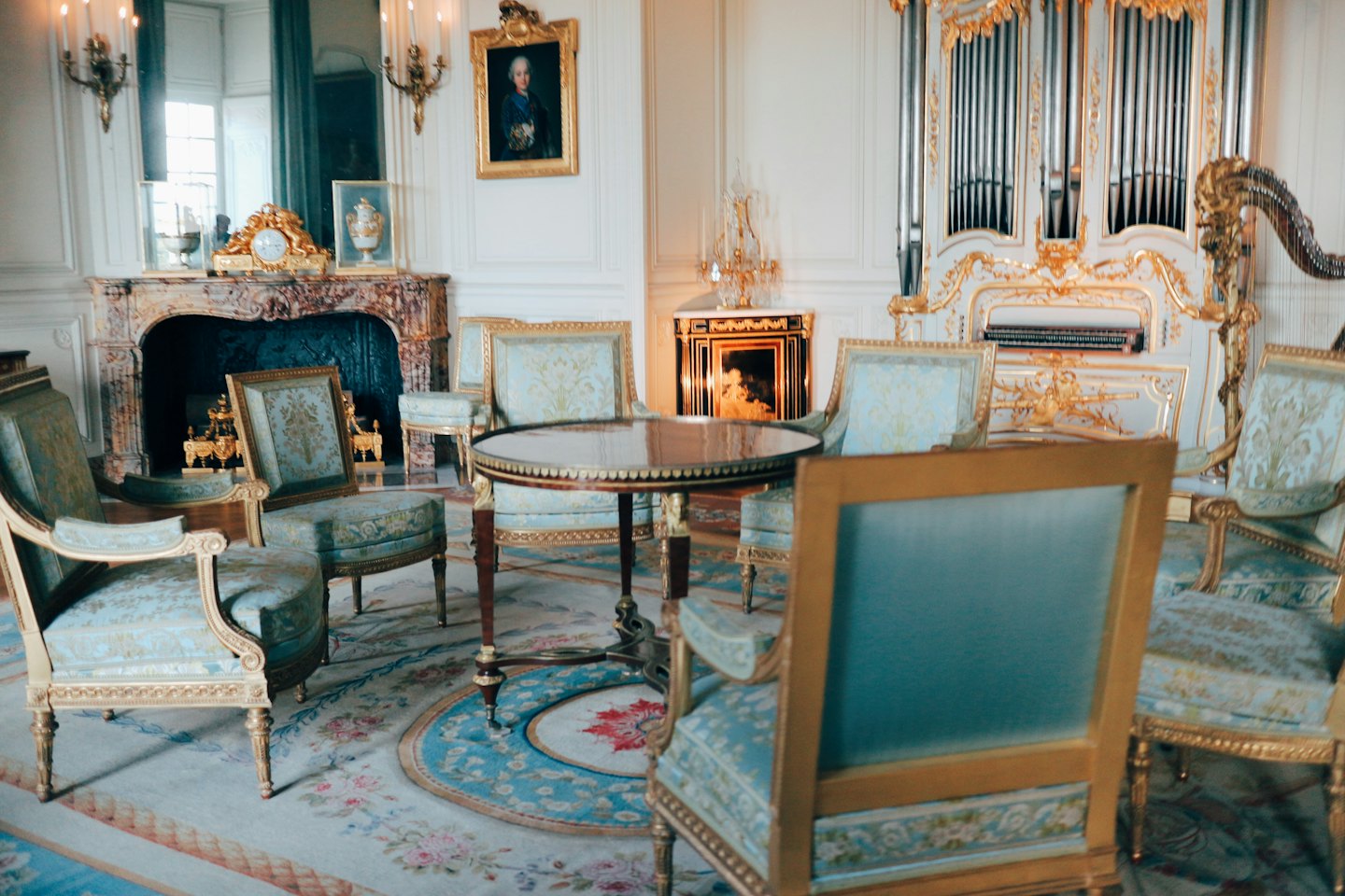 Gouden fauteuils en een sierlijk pijporgel in een luxueuze kamer in Franse stijl.