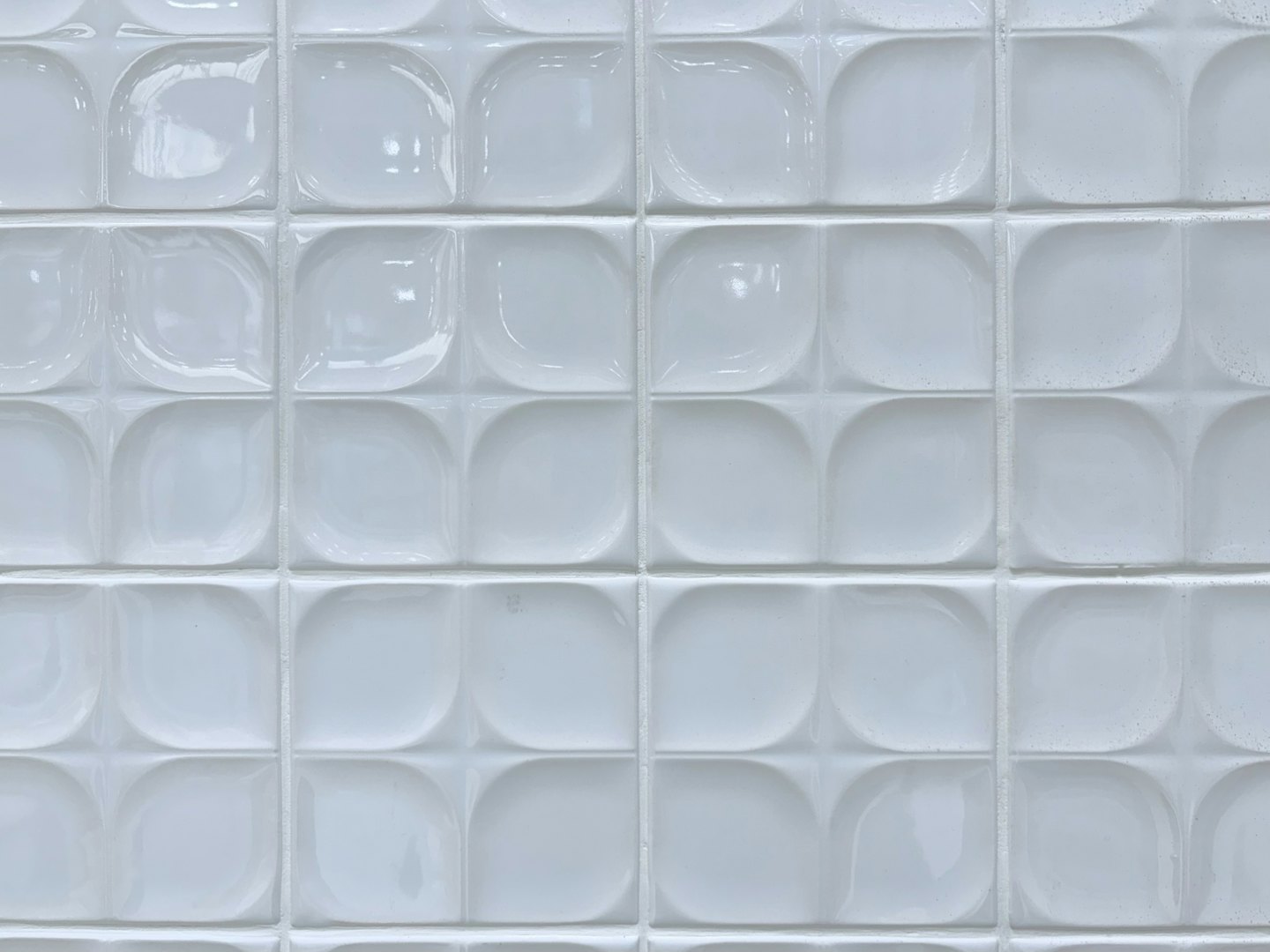 Moderne muur bedekt met glanzende witte keramische tegels met verhoogde bloemblaadjespatronen.